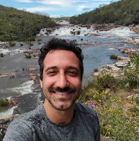 Leo selfie, smiling next to a watefall, surrounded by rocks, flowers and a clean sky